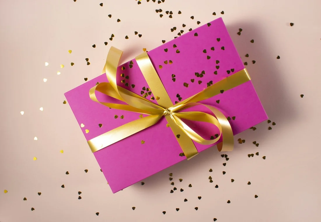 A pink gift box with a gold ribbon